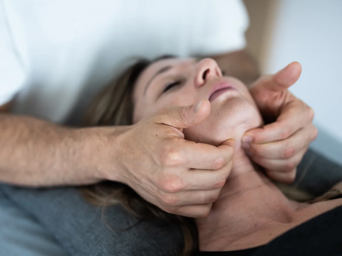 Physiotherapeut behandelt Kiefer und Halsbereich einer liegenden Patientin