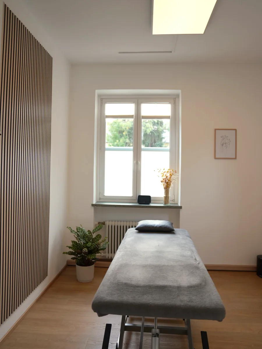 Behandlungsraum mit Liege, Fenster und Holzlamellenwand